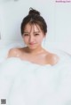 A woman is sitting in a bathtub filled with foam.