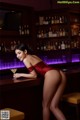 A woman in a red bodysuit leaning on a bar counter.