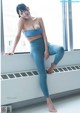 A woman in a blue sports bra top and leggings posing by a window.