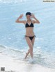 A woman in a black bikini running into the ocean.